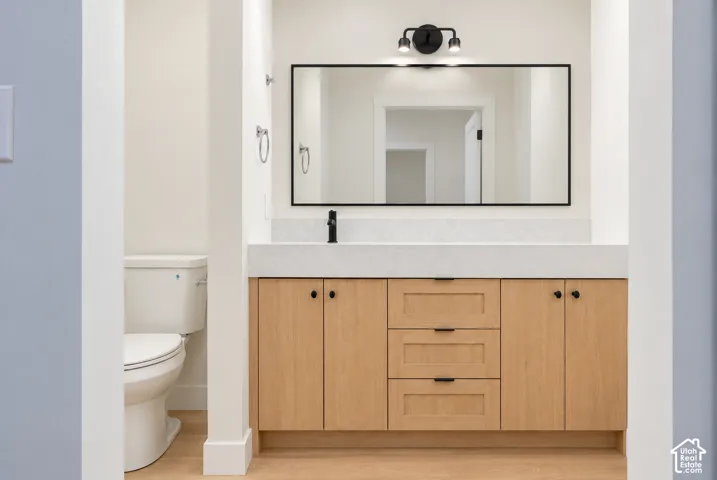 Natural wood-finish cabinetry, rectangular composite countertop with integrated sink, matte black hardware, dual-light fixture, and rectangular mirror with a black frame Virtually Staged