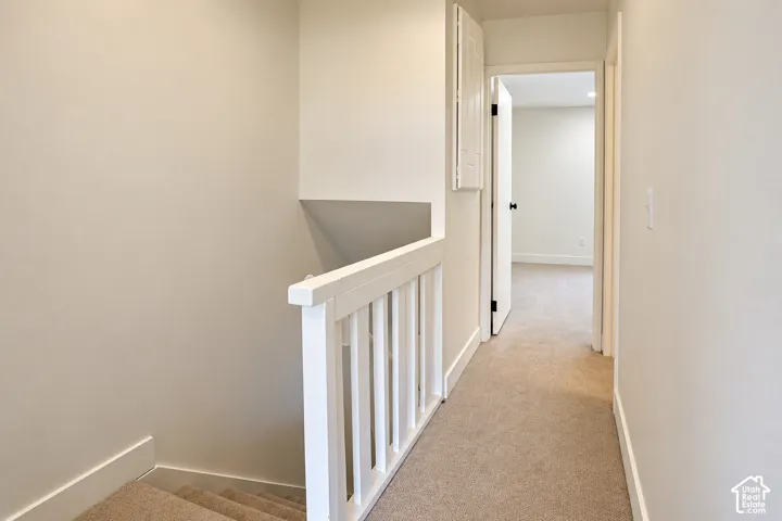 Neutral interior hallway featuring carpeted flooring, white wooden stair railing, and crisp painted walls