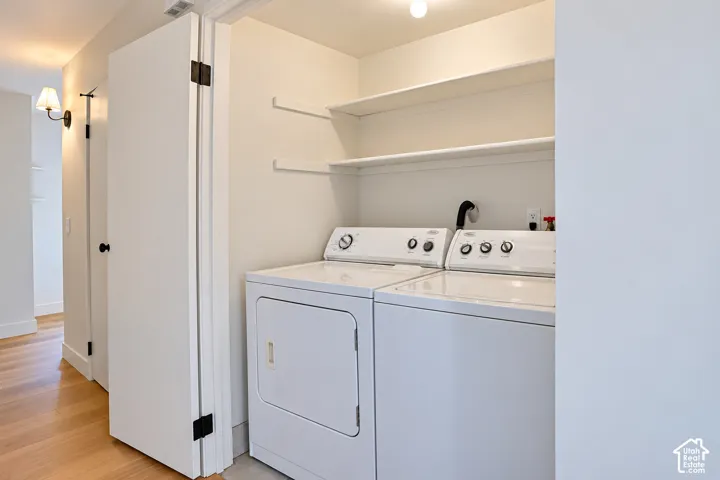 Laundry closet featuring built-in shelving, white-finish cabinetry, and wood-finish flooring