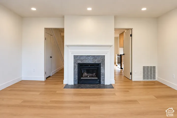 Fireplace featuring a classic white mantel, stone-tile surround, and dark hearth, complemented by recessed lighting and wood-finish flooring