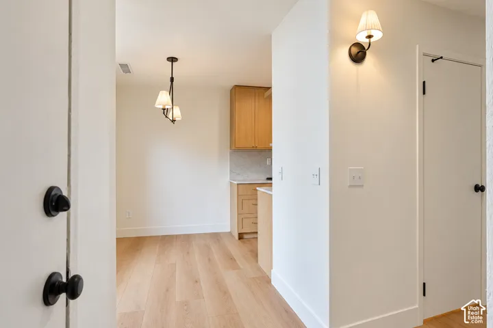 Wood-finish flooring, light-toned custom cabinetry, stone-finish backsplash, multi-arm chandelier, and wall-mounted sconce lighting