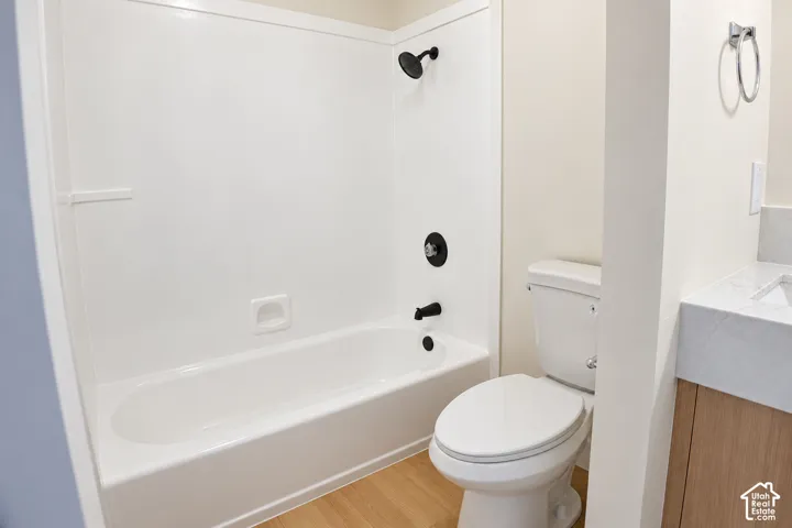 Full bathroom featuring a tub-shower combination with matte black fixtures, wood-finish flooring, a vanity with a white countertop, and a wall-mounted towel ring