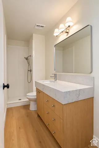 Bathroom featuring a wood-finish vanity with a stone-composite countertop, integrated sink, rectangular wall mirror with rounded corners, and a walk-in shower stall