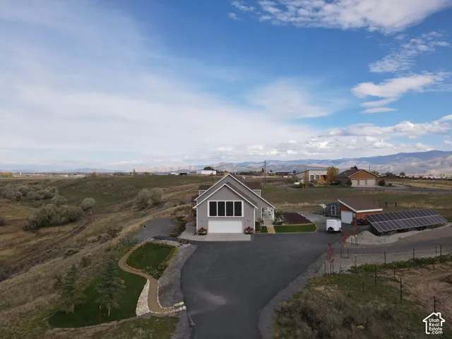 Gable-roof exterior featuring an attached two-car garage, expansive asphalt driveway, ground-mounted solar array, and established tiered landscaping