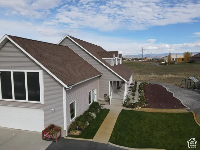 Multi-level exterior featuring light gray horizontal siding, asphalt shingle roofing, integrated solar panels, concrete driveway, and landscaped garden beds