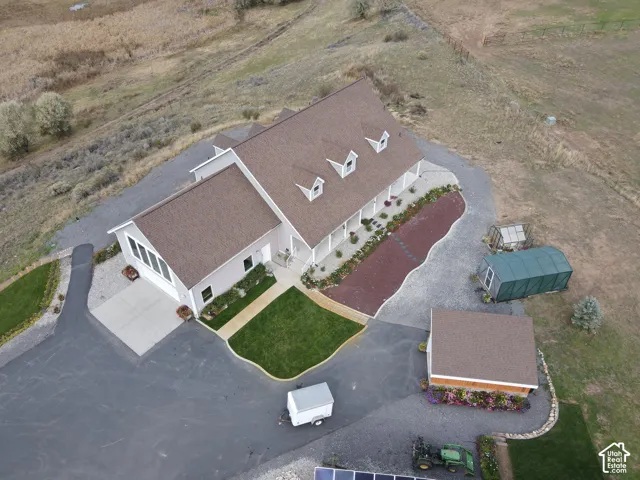 Aerial view of a sprawling property featuring a multi-gabled residence with dormer windows, an extensive covered porch, an attached multi-car garage, a detached storage building, and paved driveway surfaces