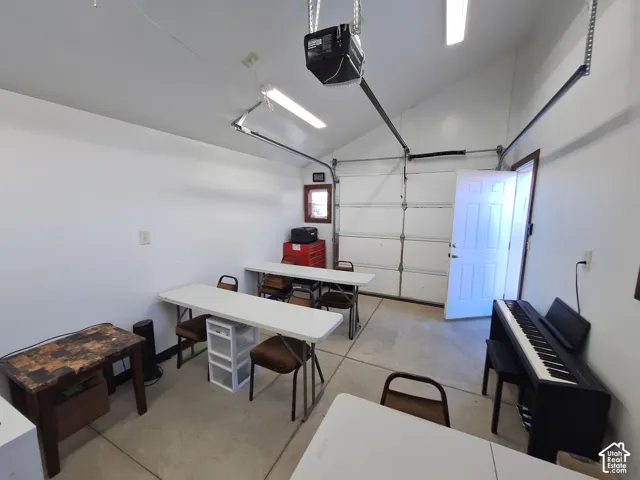 Garage space featuring vaulted ceilings, linear fluorescent lighting, epoxy flooring, and a six-panel exterior entry door