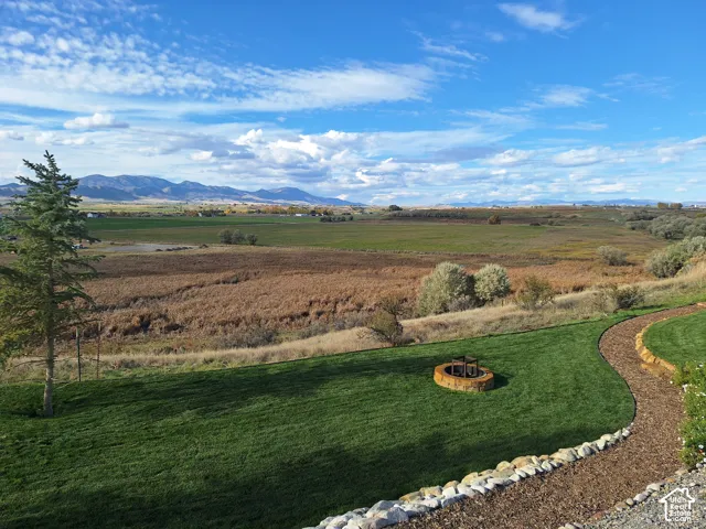 Expansive landscaped grounds featuring a circular stone fire pit, tiered rock retaining walls, and a dedicated stone-path walkway, set against a backdrop of distant mountain ranges and open fields