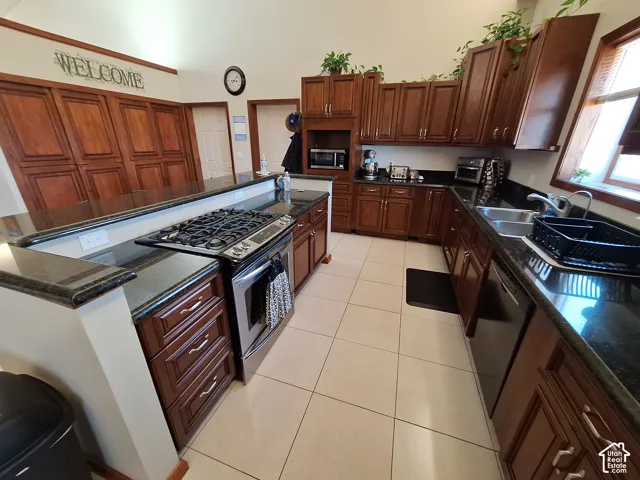 Kitchen featuring stained wood cabinetry, granite countertops, stainless steel gas range, large-format tile flooring, and vaulted ceiling