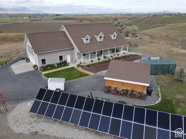 Multi-level residence featuring an asphalt shingle roof with dormer windows, a ground-mounted solar panel array, a detached structure with wood-finish siding, and a concrete driveway