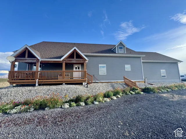 Exterior featuring horizontal vinyl siding, dual-gable covered porch with exposed wood beam accents, multi-slope asphalt shingle roof, and gravel ground cover with established floral landscaping