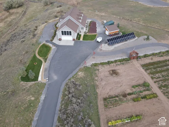 Aerial perspective of a multi-structure property featuring an expansive asphalt driveway, ground-mounted solar panel array, attached garage, and manicured landscaping