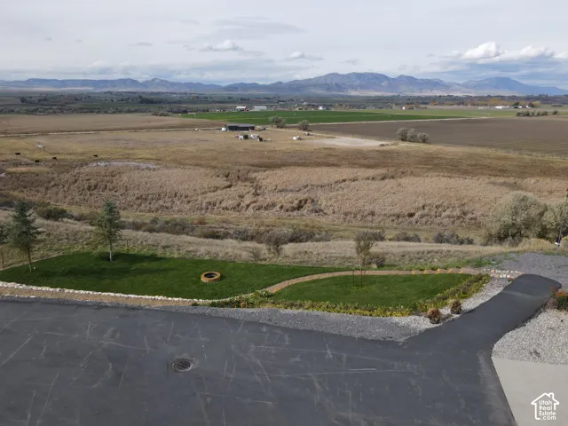Expansive outdoor area featuring a manicured lawn, stone-lined fire pit, asphalt driveway, and mountain backdrop