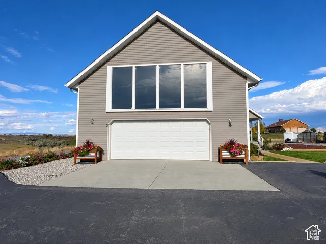 Gable-roof exterior featuring neutral horizontal siding, an oversized four-panel window configuration, and a double-bay garage with a paved concrete apron