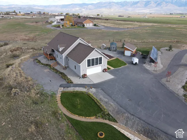 Aerial perspective of a multi-structure property featuring a detached garage, solar panel array, paved driveway, landscaped lawn areas with stone-bordered pathways, and a mountain backdrop