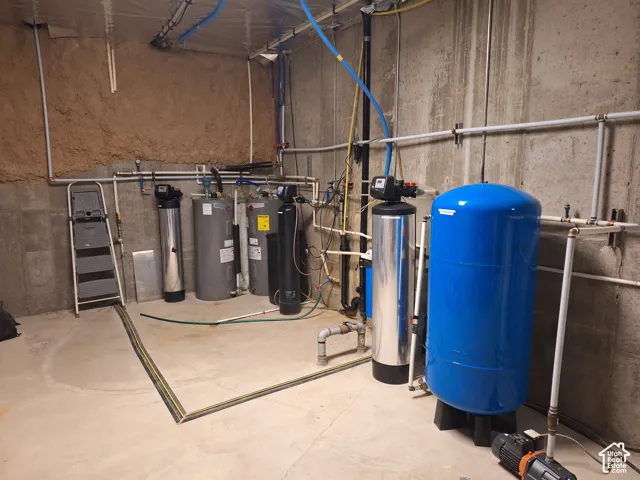 Mechanical utility area featuring a water pressure tank, multi-stage water filtration system, and two water heaters with exposed concrete foundation walls