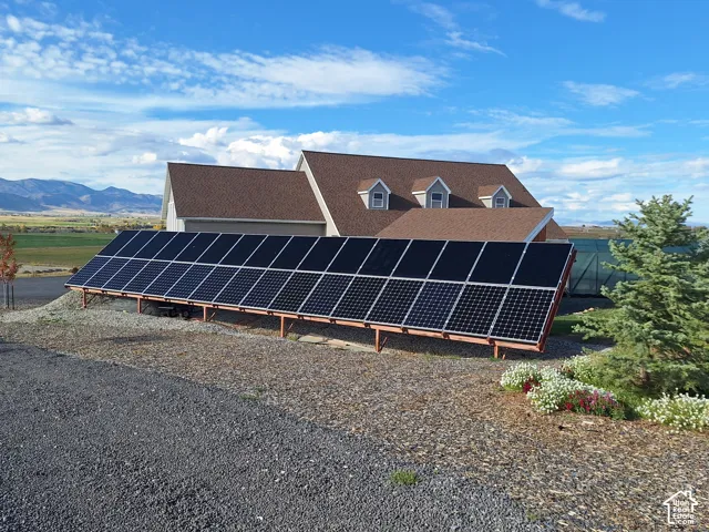 Ground-mounted solar array, shingle roofing, dormer windows, and mountain backdrop