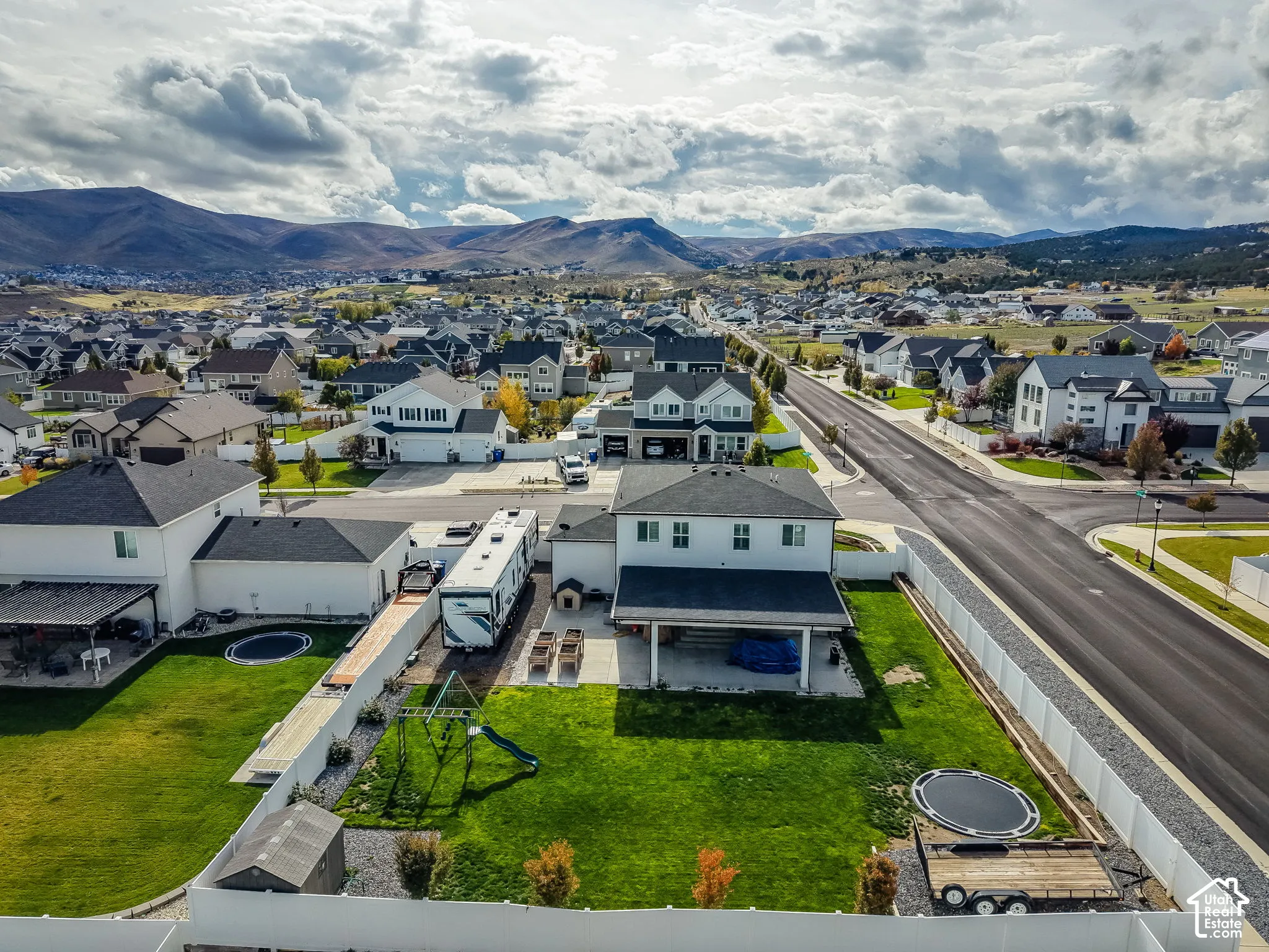Aerial perspective of a two-story residence featuring a covered rear patio, a fenced backyard, and mountain backdrops