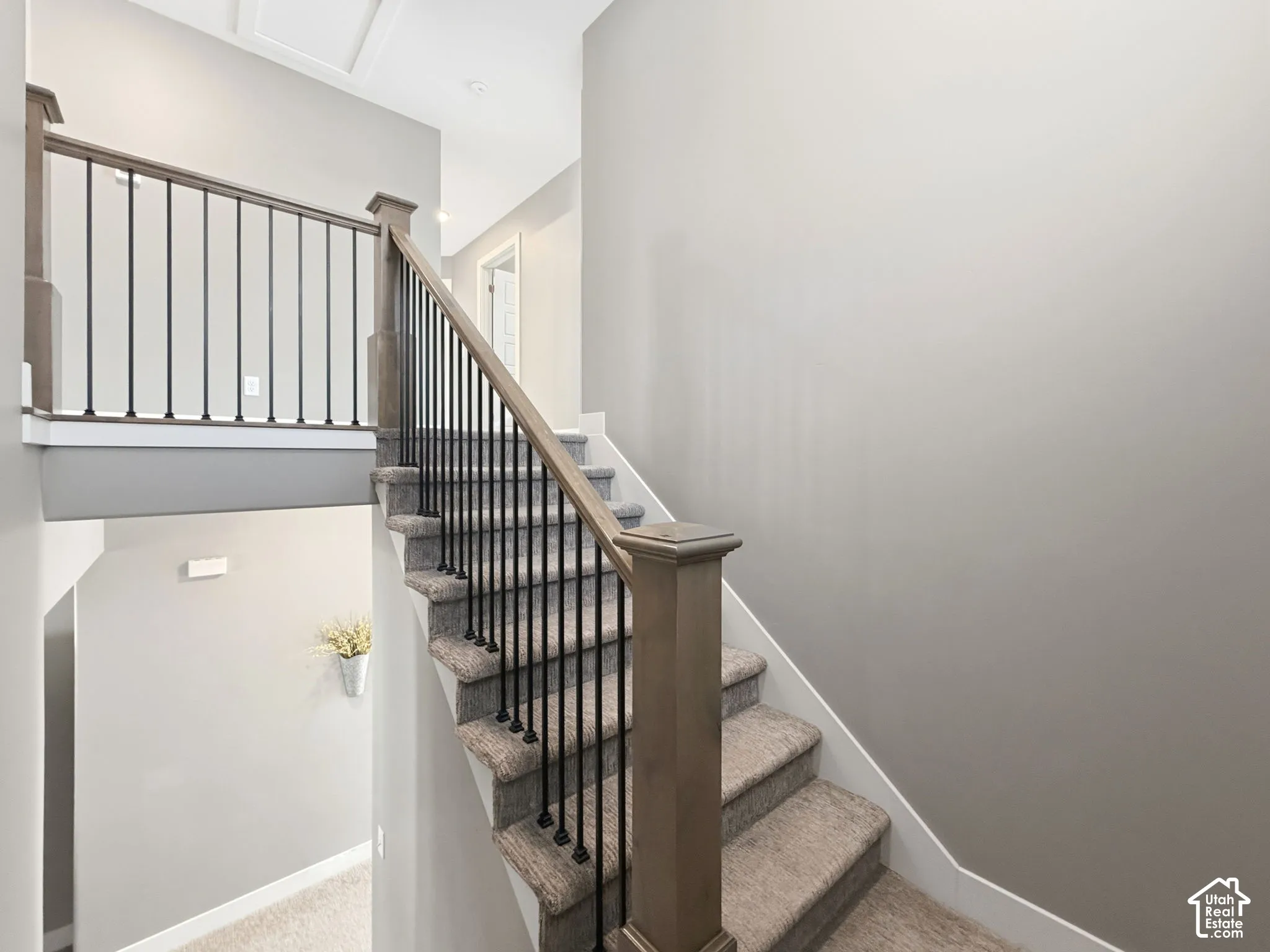 Staircase featuring carpeted treads, wood-finish newel posts and handrails, and vertical metal balusters