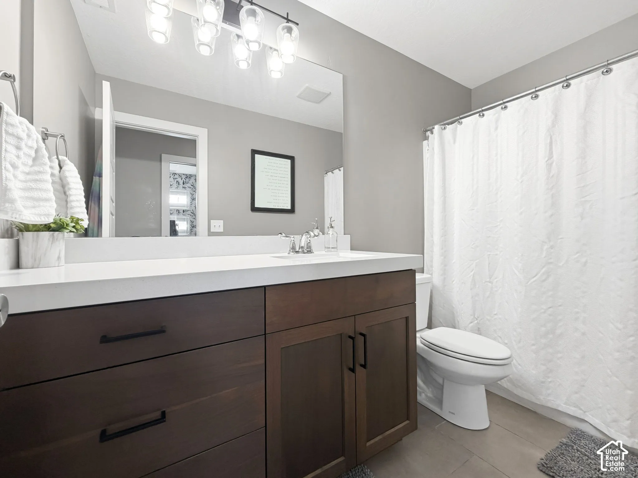 Bathroom featuring a dark wood-finish vanity with matte black hardware, a solid surface countertop with integrated basin, and a five-bulb vanity light fixture