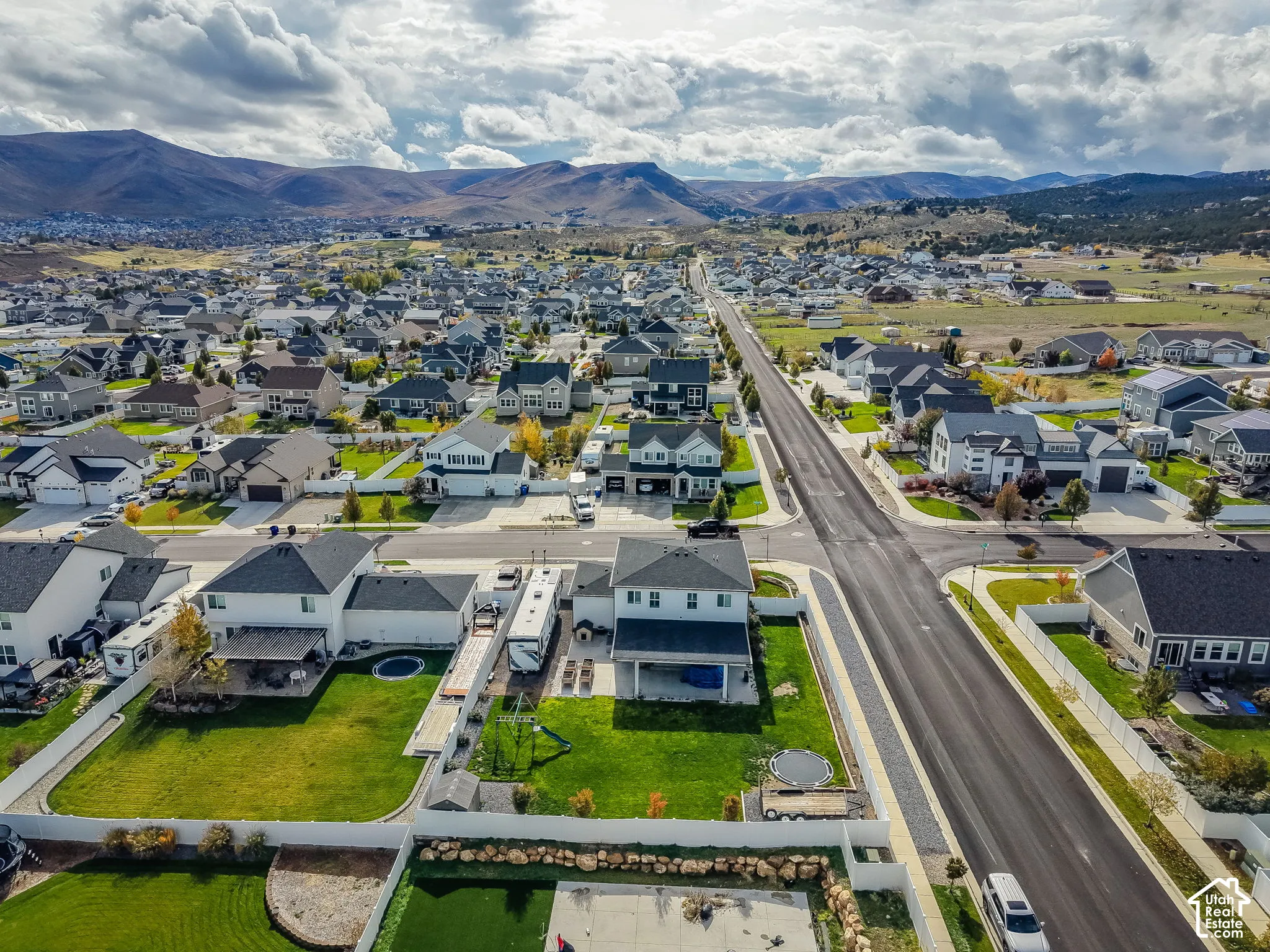 Aerial perspective featuring a two-story residence with a covered patio, fenced backyard, lawn, and mountain backdrop