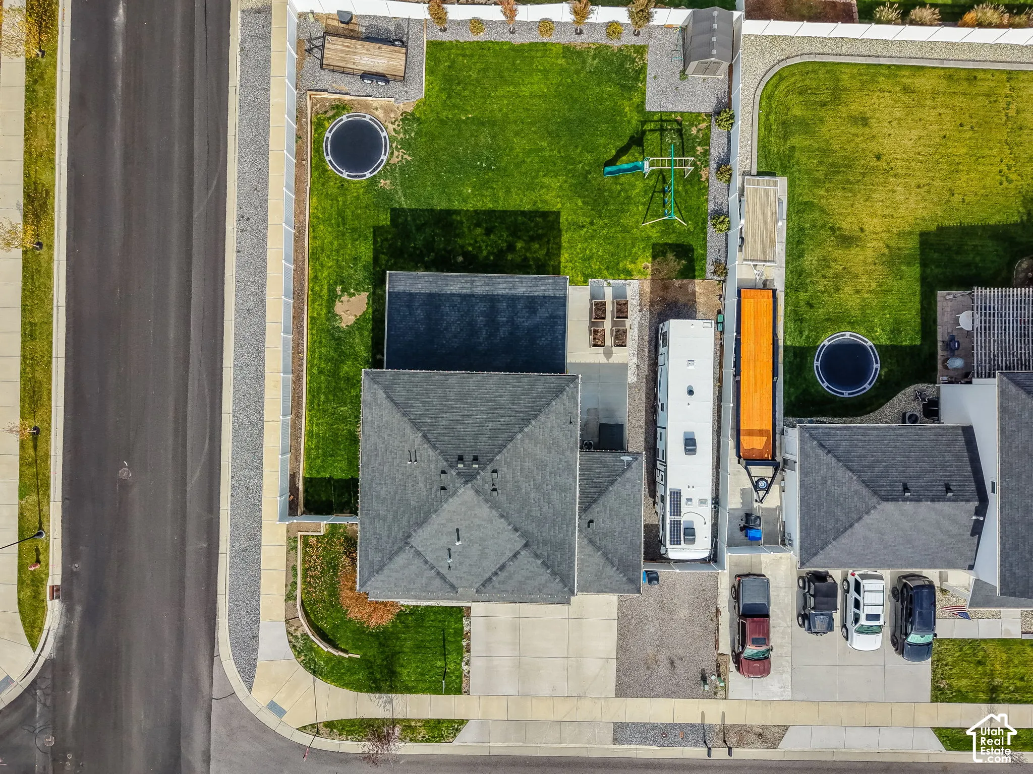 Aerial perspective of a corner lot property featuring a fully fenced backyard, a concrete patio, and a side-yard concrete pad