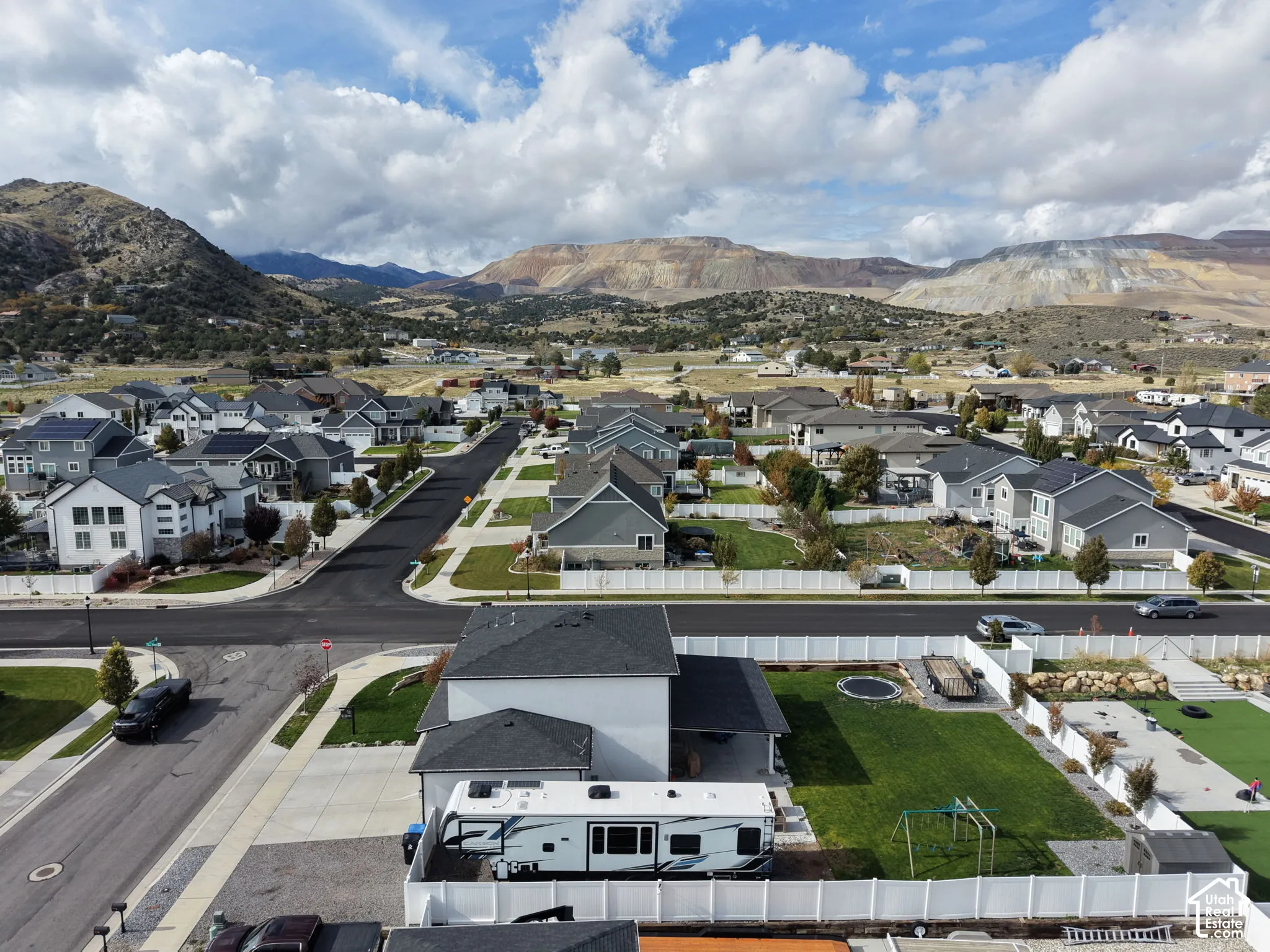 Aerial perspective featuring a multi-story residence with a paved driveway, private fenced backyard, manicured lawn, and expansive mountain scenery
