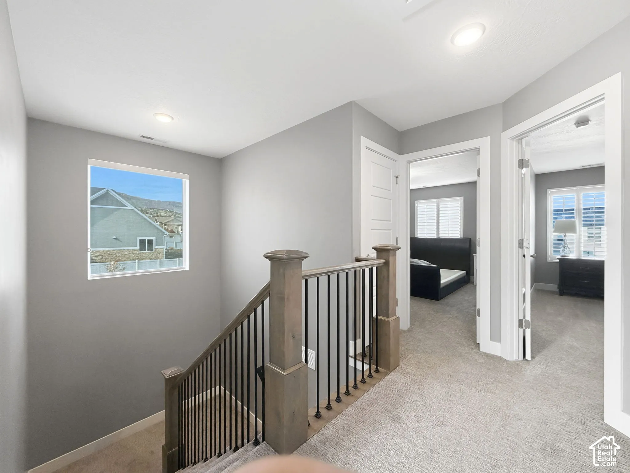 Staircase featuring wood handrails, square newel posts, and matte black metal balusters, complemented by wall-to-wall carpeting and recessed lighting