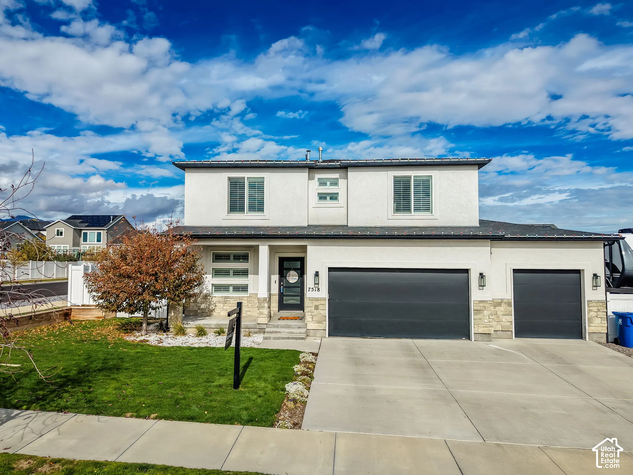 Two-story residence featuring a smooth stucco exterior, stone veneer accents, multi-pane windows, a recessed entry, and an attached three-car garage