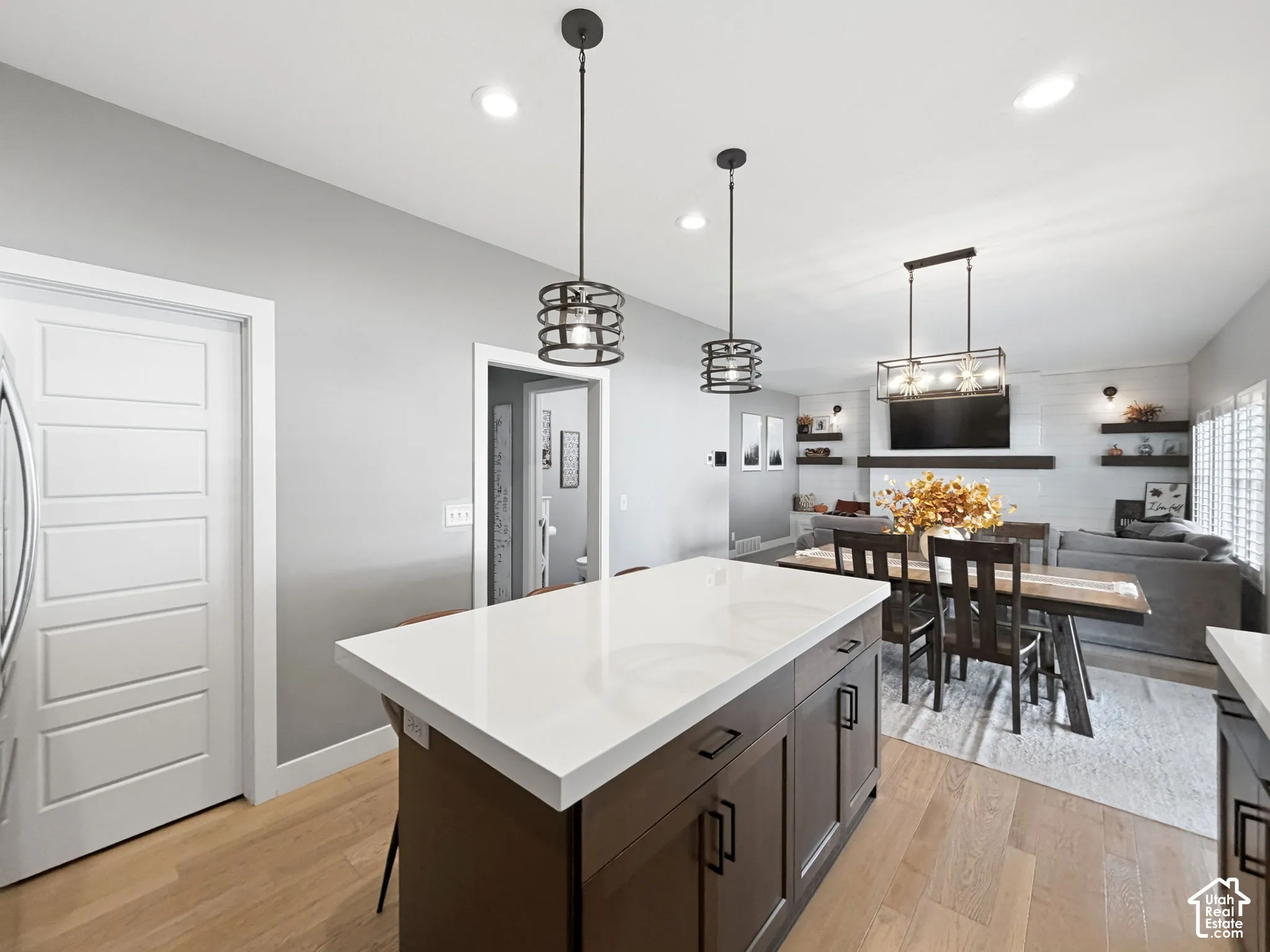 Kitchen island featuring a quartz countertop and dark cabinetry, complemented by recessed lighting, dual cage-style pendant lights, and light-tone wood-finish flooring
