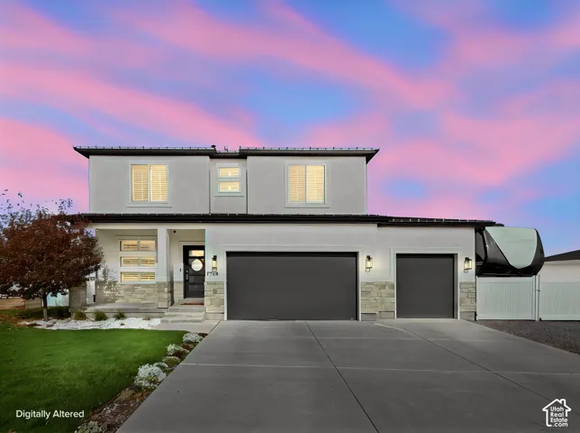 Modern exterior featuring smooth-finish siding with stone veneer accents, a triple-pane window entry door, a multi-car garage, and integrated wall-mounted exterior lighting