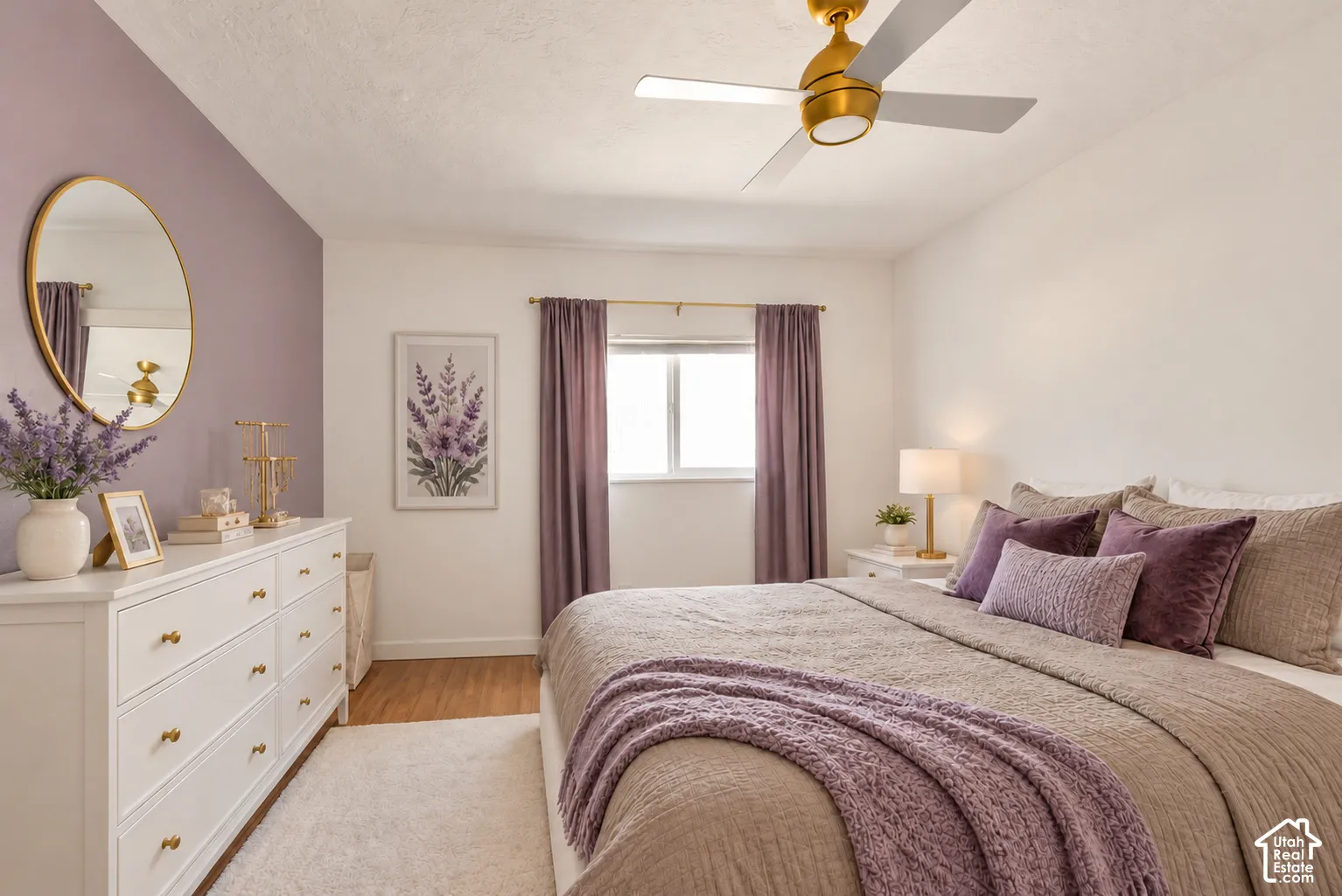 Bedroom featuring wood-finish flooring, a matte gold finish ceiling fan with integrated lighting, and a neutral color palette with a single accent wall