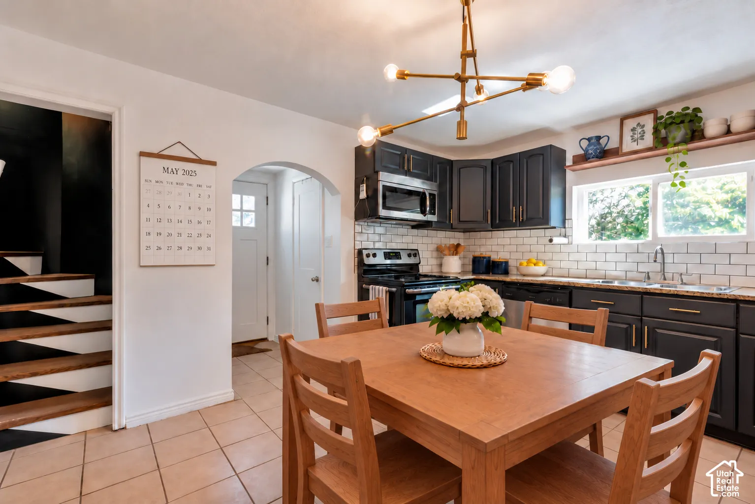 Kitchen featuring dark cabinetry, stone countertops, a white subway tile backsplash, a multi-arm brass light fixture, and tile flooring