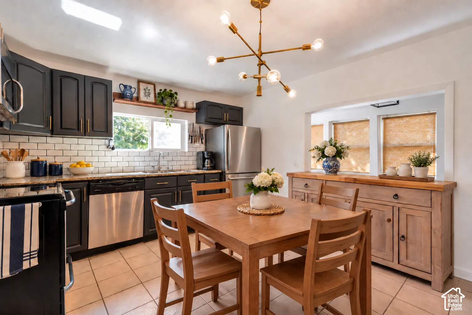 Kitchen featuring dark shaker-style cabinetry, a white subway tile backsplash, stainless steel appliances, a brass sputnik-style chandelier, and tile flooring