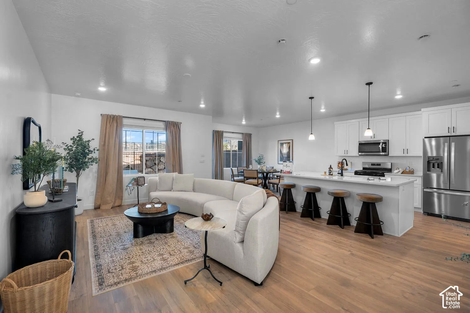 Open-concept living space featuring wood-finish flooring, a kitchen island with stone-composite countertop, white shaker-style cabinetry, and recessed lighting