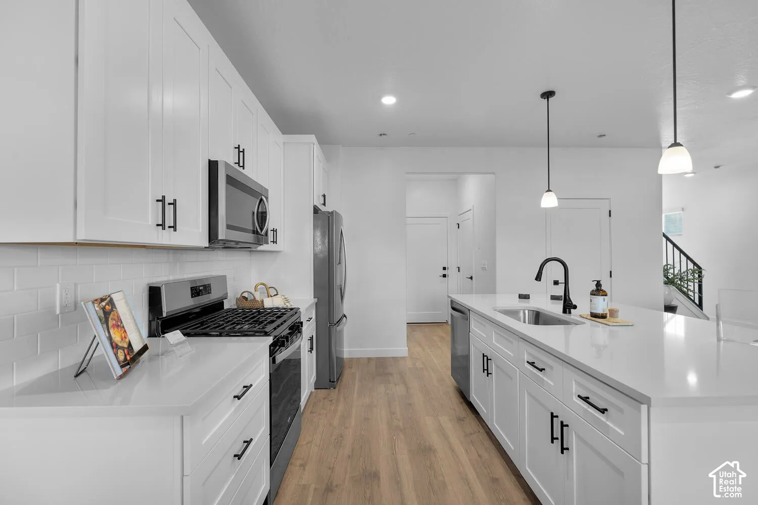 Kitchen featuring white cabinetry, quartz countertops, subway tile backsplash, stainless steel appliances, and a center island with a matte black faucet