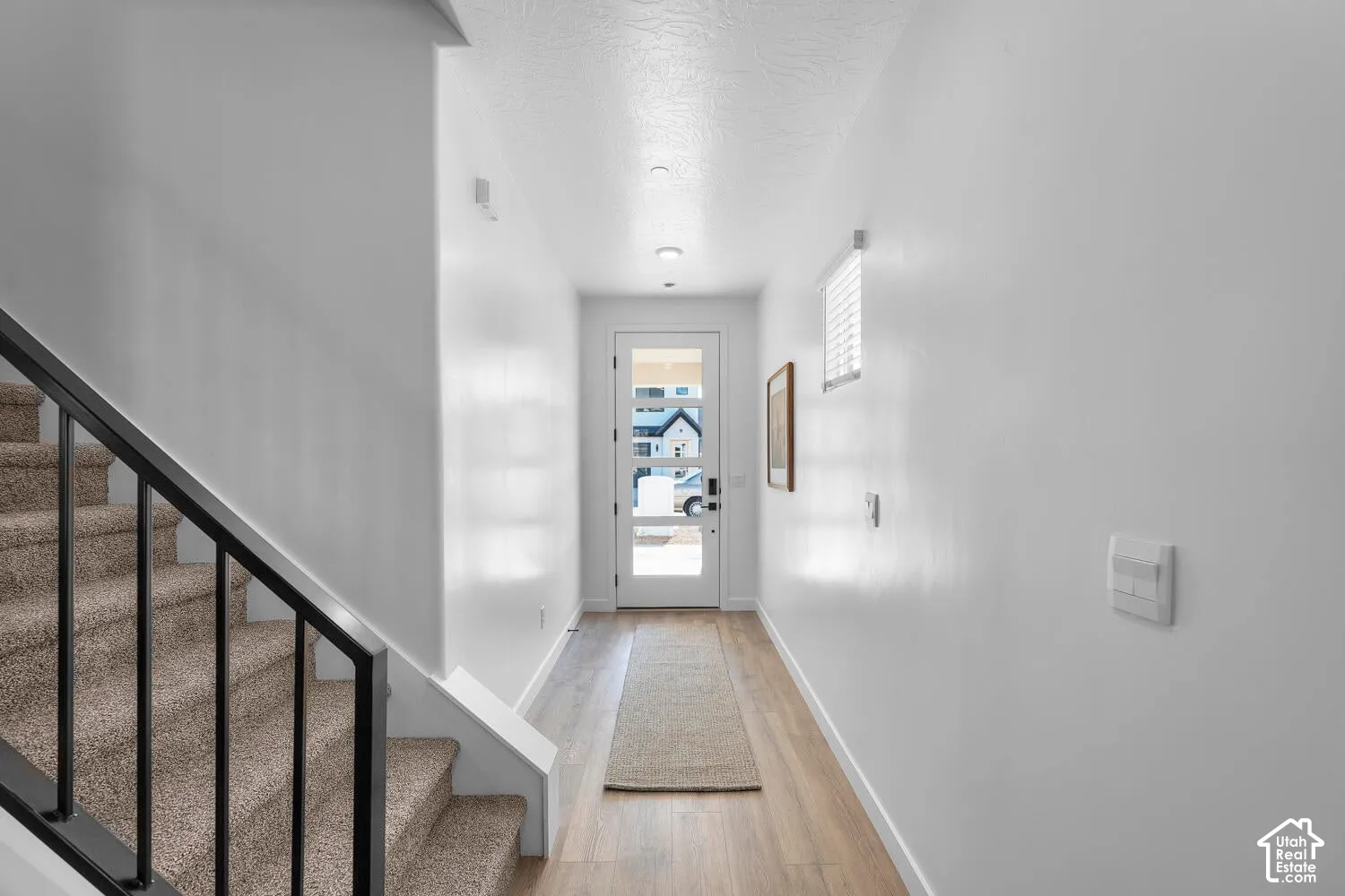 Entryway featuring wood-finish flooring, a glass-panel front door, and a staircase with a matte black metal railing