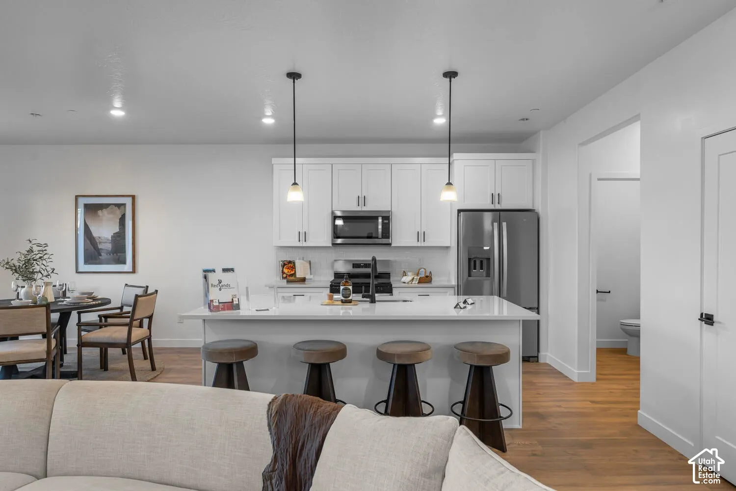 Kitchen featuring white shaker-style cabinetry, a quartz-topped island with seating, stainless steel appliances, and wood-finish flooring
