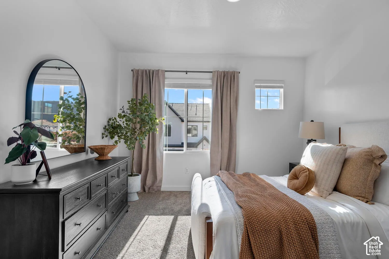 Neutral-toned carpeted flooring, large window with natural light, arched wall mirror, and recessed ceiling lighting