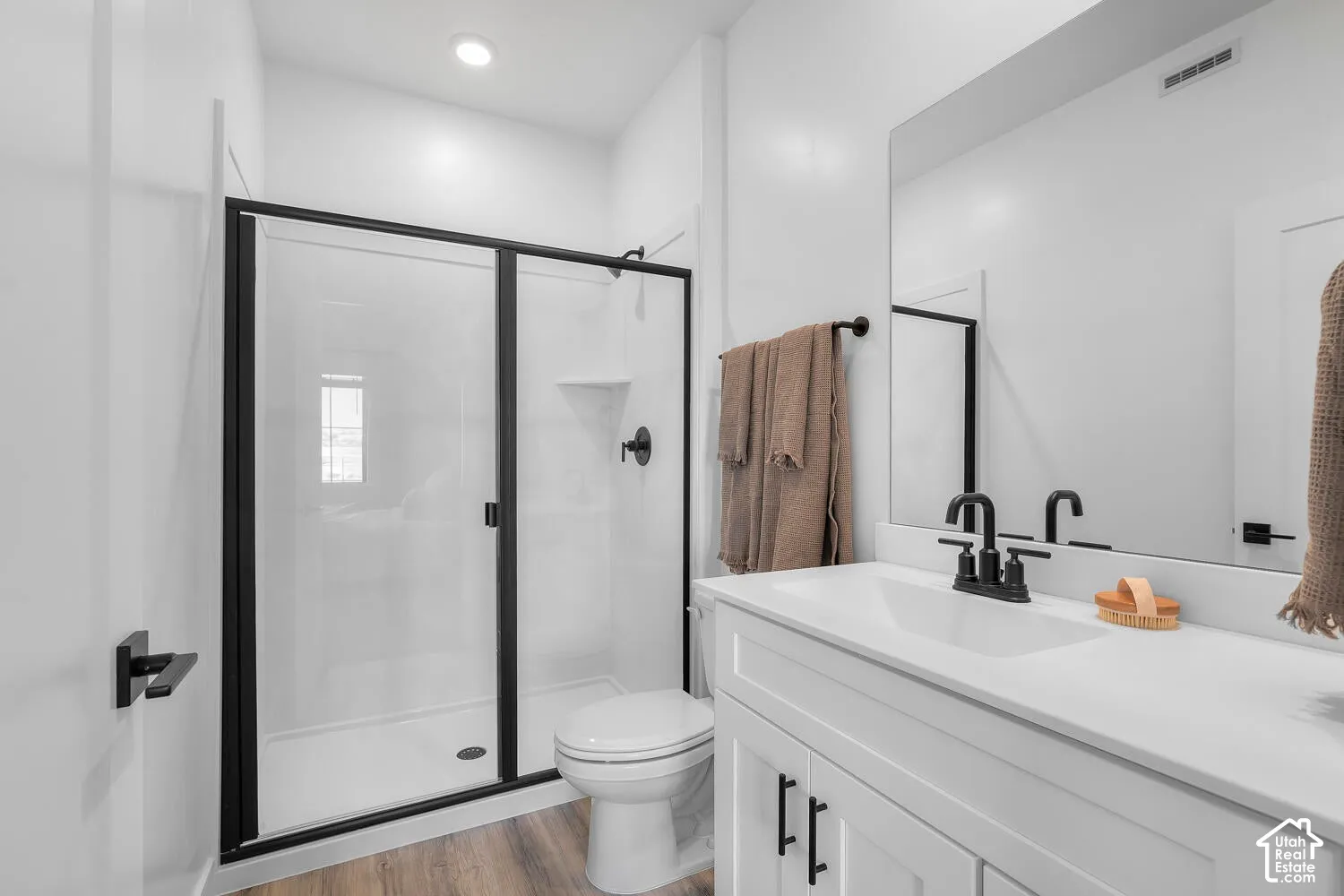 Bathroom featuring a vanity with a white countertop and basin, walk-in shower with a black-framed glass enclosure, matte black plumbing fixtures, and wood-finish flooring