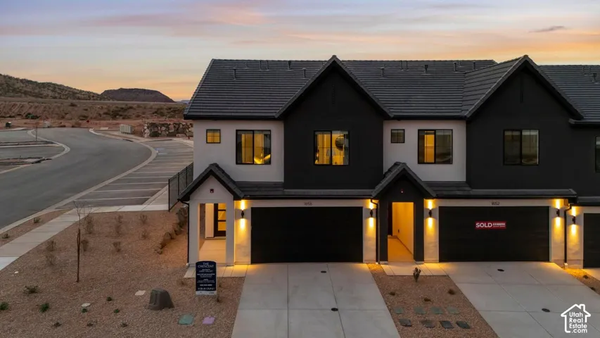Two-story townhome exterior featuring a high-contrast stucco and board-and-batten facade, concrete tile roof, dual-gabled entryways, and attached multi-car garages