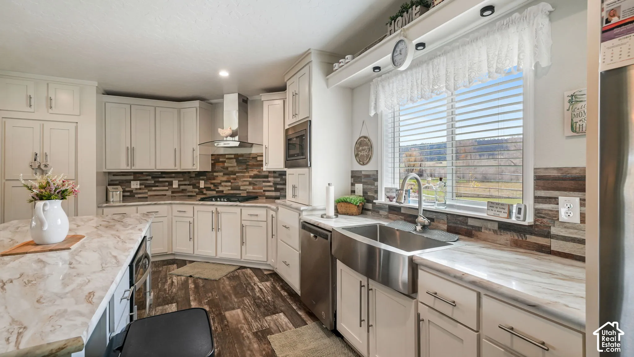Kitchen featuring white shaker-style cabinetry, stone-patterned countertops, stainless steel farmhouse sink, tile backsplash, and wood-finish flooring