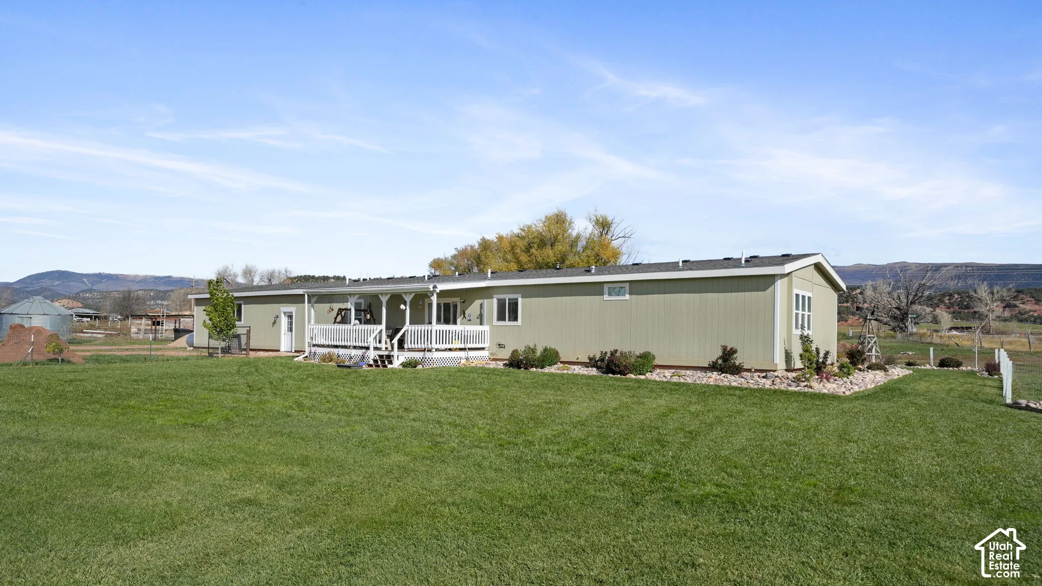 Exterior featuring horizontal siding, a covered porch with white railing, and a sprawling lawn accented by decorative stone landscaping