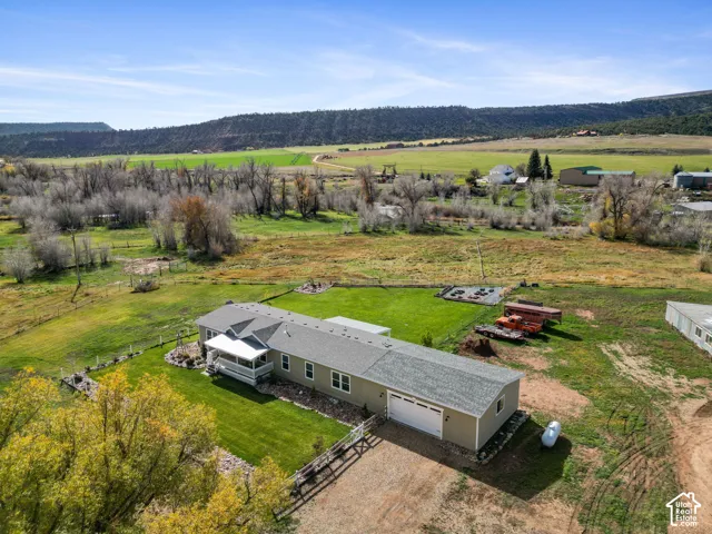 Single-story residence featuring an attached two-car garage, covered porch, manicured lawn, and extensive acreage set against a mountain backdrop