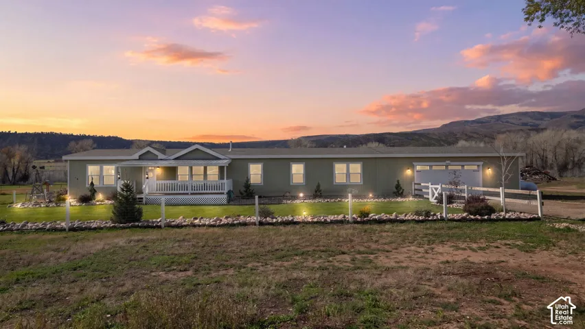 Single-level exterior featuring horizontal siding, a covered front porch with white railing, an attached garage, and a fenced yard with mountain backdrop