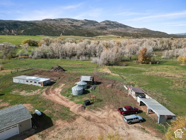 Expansive acreage featuring mountain scenery, metal outbuildings, dual grain silos, and a covered shed structure