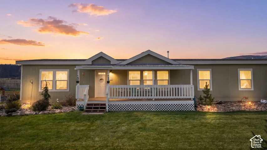 Single-story exterior featuring wood-style siding, a covered front porch with white railing, and decorative lattice skirting set against a backdrop of distant mountains
