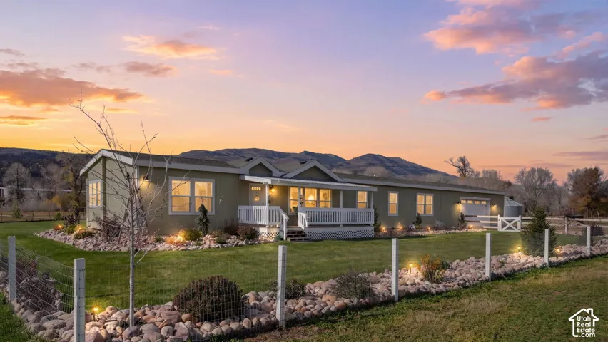 Single-story exterior featuring a covered front porch, white railing, attached garage, rock landscaping beds, and a perimeter fence
