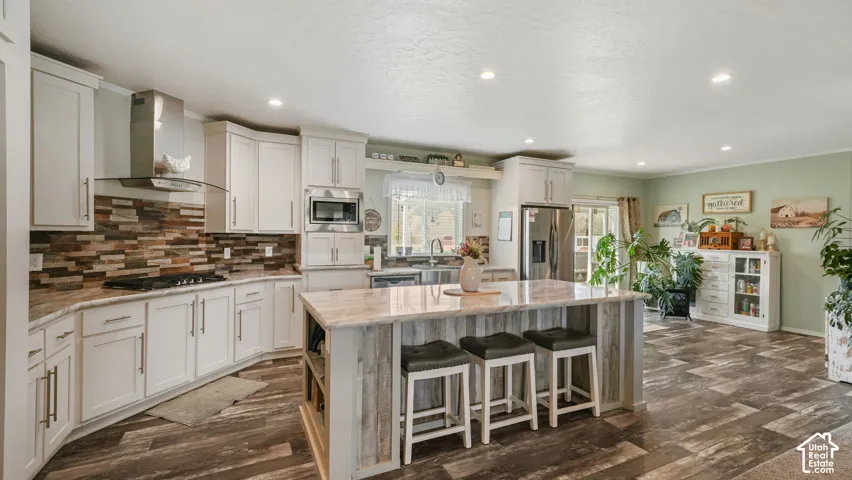 Kitchen featuring white cabinetry, stone-veneer backsplash, central island with stone-finish countertop, wood-finish flooring, and stainless steel appliances