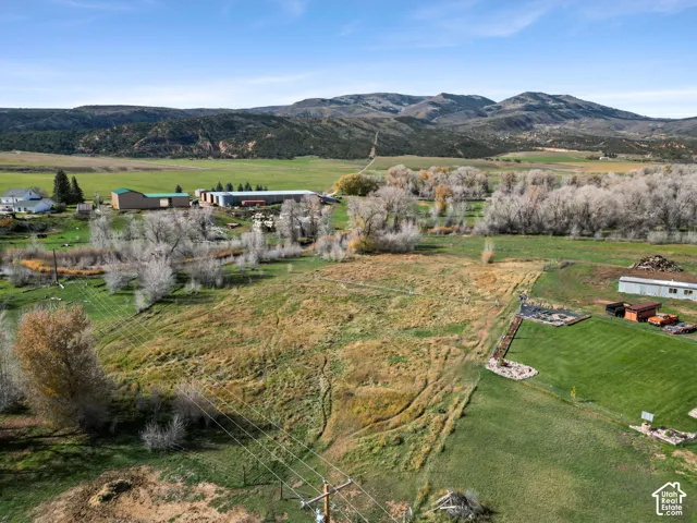 Expansive acreage featuring native pastureland, mature deciduous trees, a maintained grass lawn, and prominent mountain backdrops